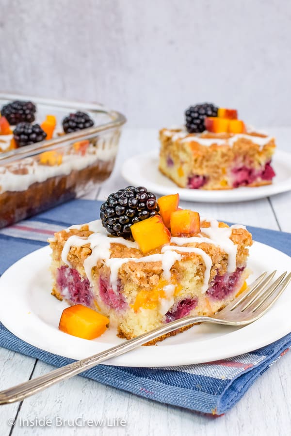 Two white plates with squares of peach blackberry coffee cake with fresh fruit on them.