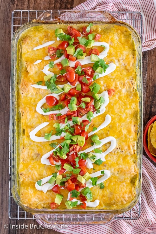 An overhead picture of a baking dish filled with easy chicken enchiladas and topped with sour cream, avocado, and tomatoes.