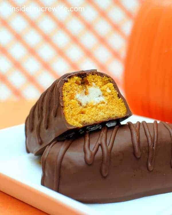 Chocolate covered pumpkin twinkies on a plate. One cut open to show the filling.