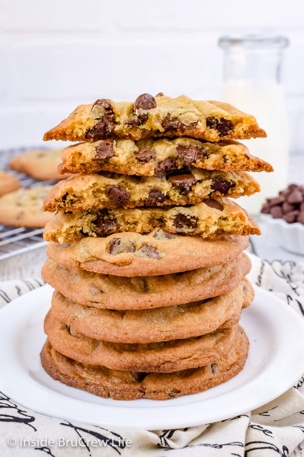 A white plate with a stack of chocolate chip cookies on it topped with more cookies broken in half.