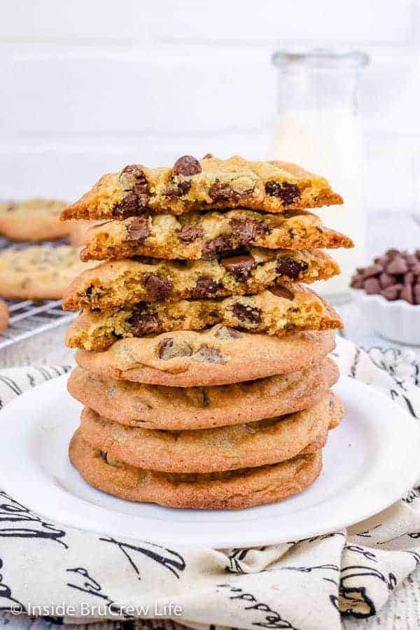 A stack of chocolate chip cookies on a white plate with a few cookies broken in half on top.