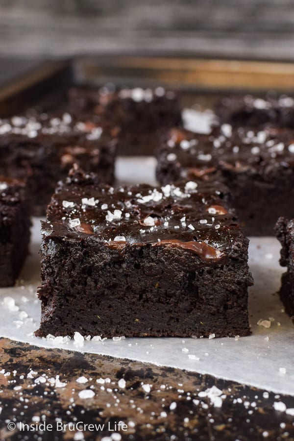 Close up picture of a dark chocolate zucchini brownie on a tray with more brownies behind it