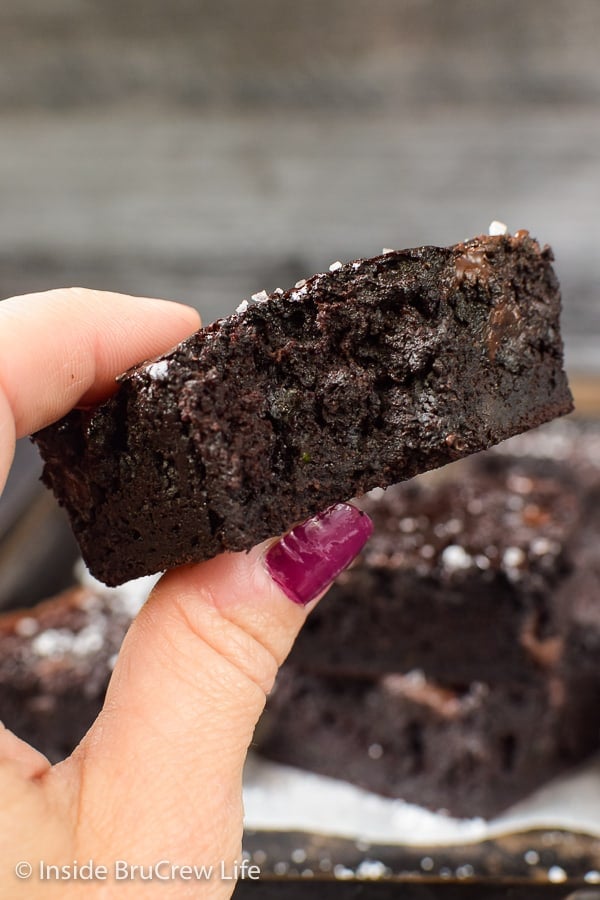 A hand holding a dark chocolate zucchini brownie up close with a bite out of it