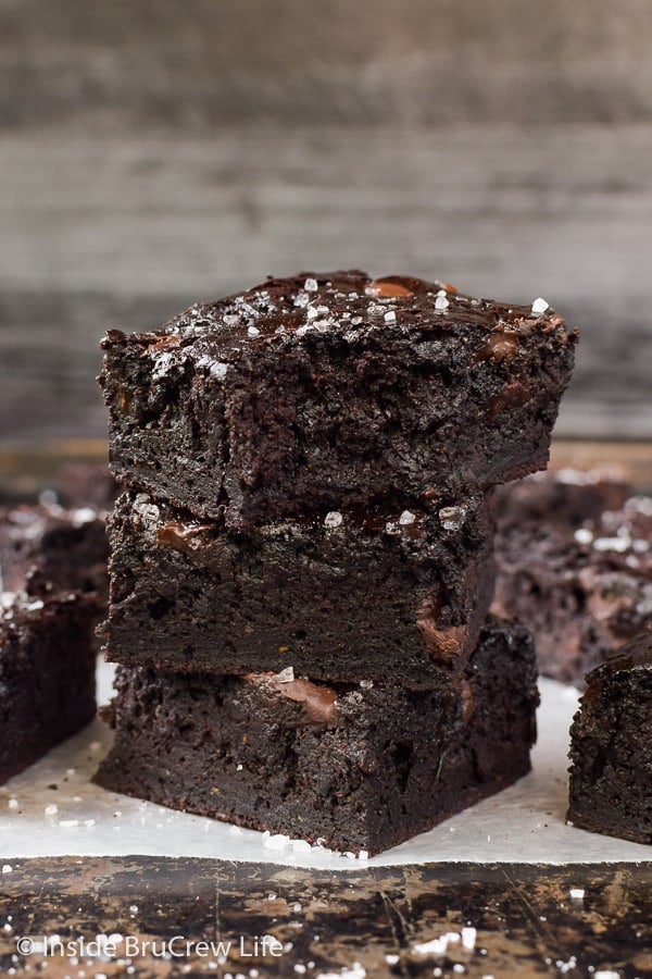 A stack of three dark chocolate zucchini brownies on a try with a bite out of the top one
