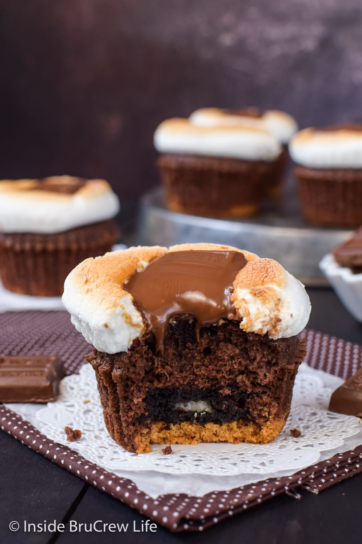 A brownie cupcake with gooey marshmallow and chocolate on top with a bite out of it.