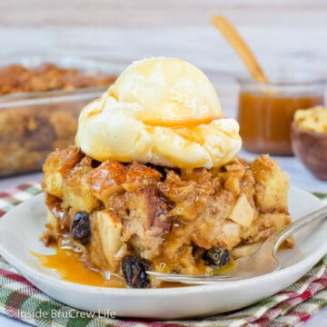 A white plate with a square of bread pudding with apples and raisins topped with ice cream on it