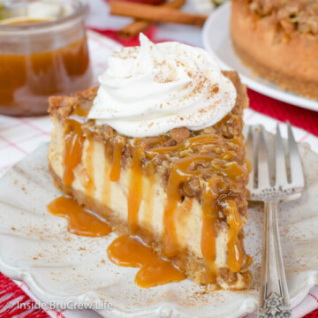 A white plate with a slice of apple cheesecake topped with a crisp topping, caramel, and whipped cream.
