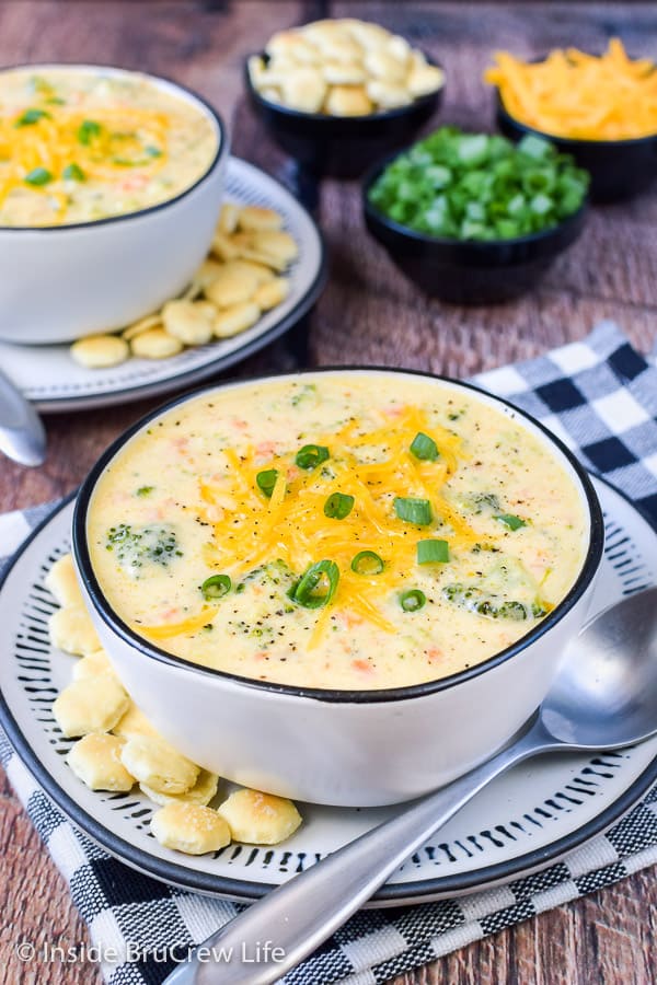 A white bowl filled with broccoli cheese soup topped with cheese and green onions.
