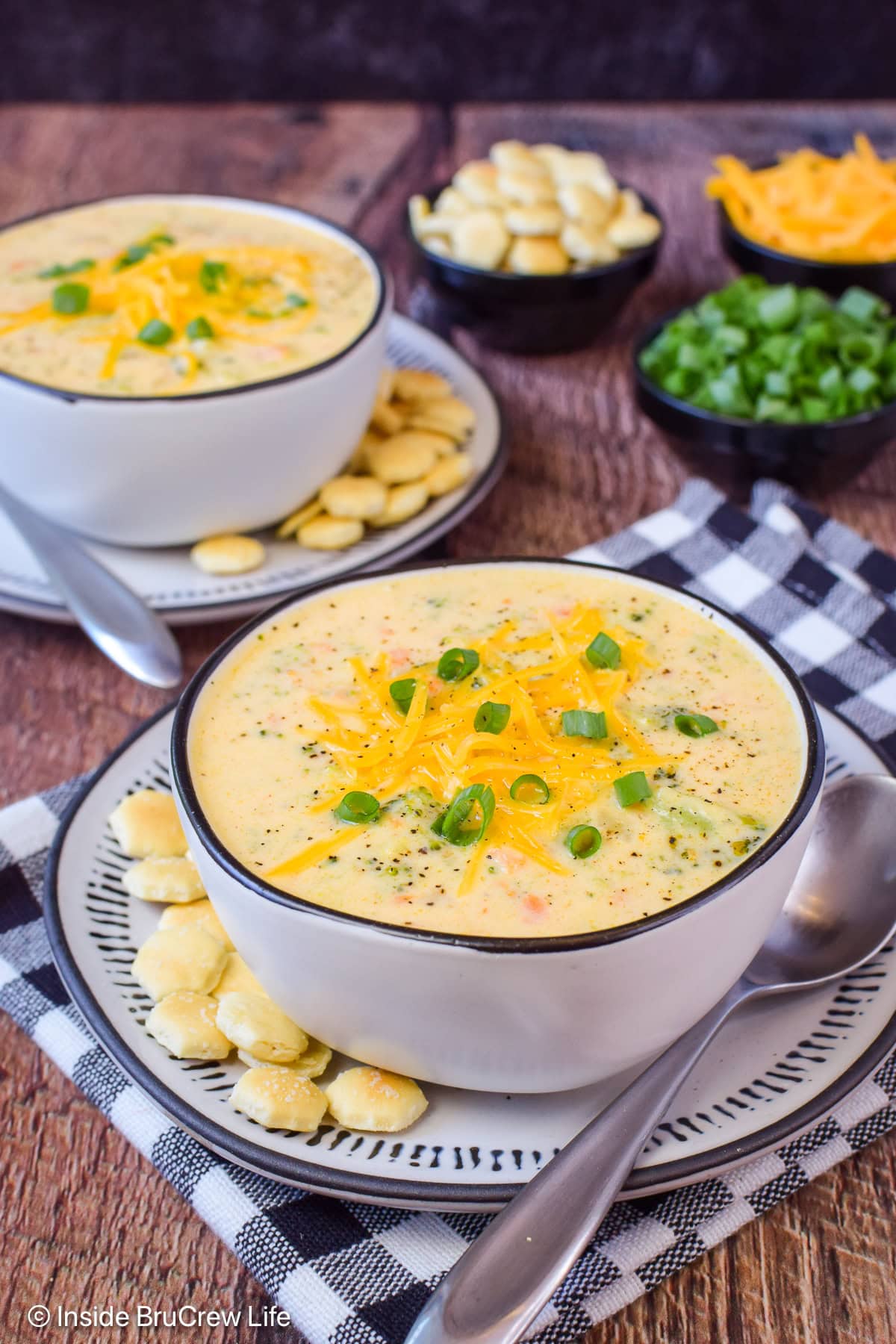 Two bowls of cheese and broccoli soup topped with cheese and onions.