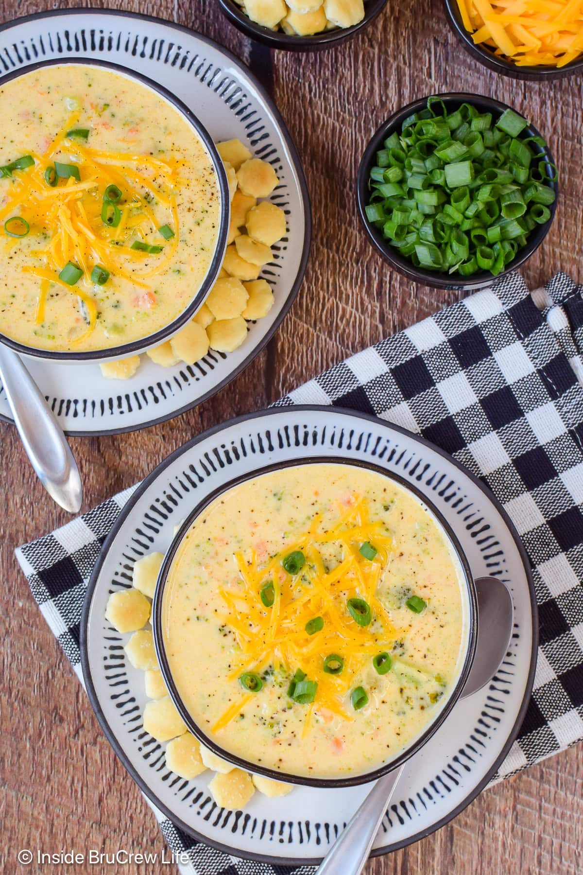 Two bowls of cheddar cheese soup with broccoli on a brown board.