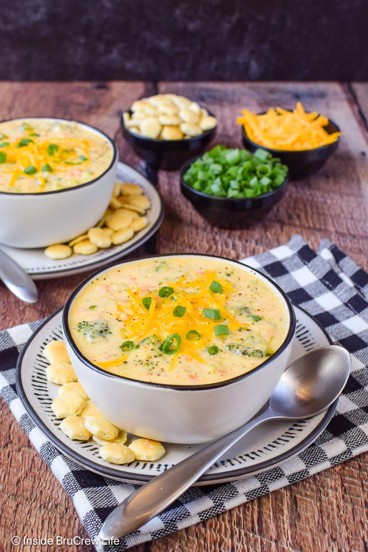 White bowls filled with a creamy cheesy broccoli soup on a brown board.