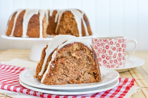 A piece of caramel apple bundt cake with apple cider glaze on a white plate and the rest of the cake behind it.