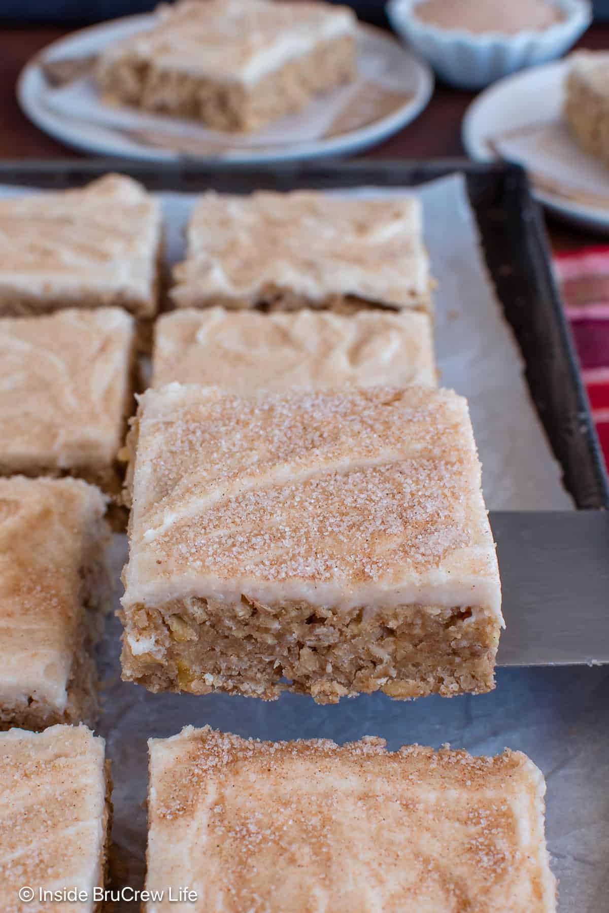 A spatula lifting a cinnamon apple bar off a sheet pan.