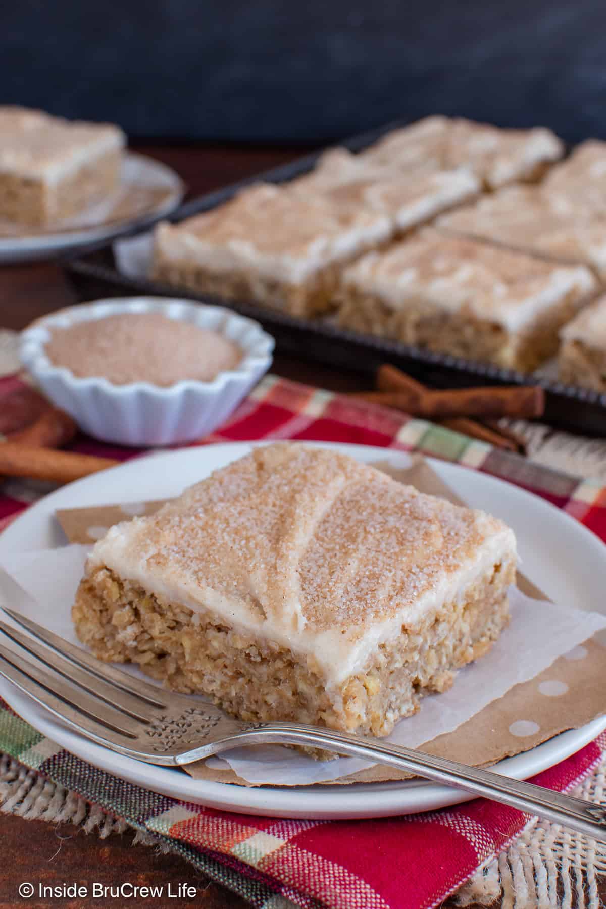 A slice of frosted cinnamon apple bar on a plate with a fork.