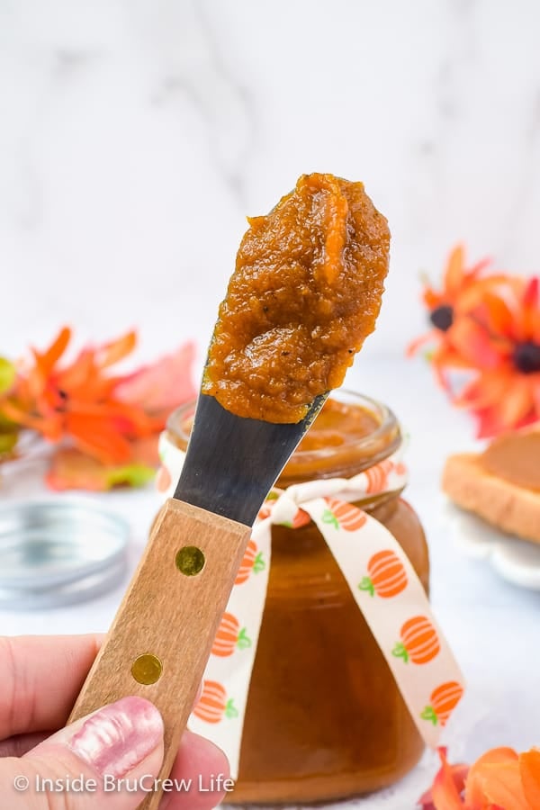 A wooden spatula with pumpkin butter held up in front of a jar.
