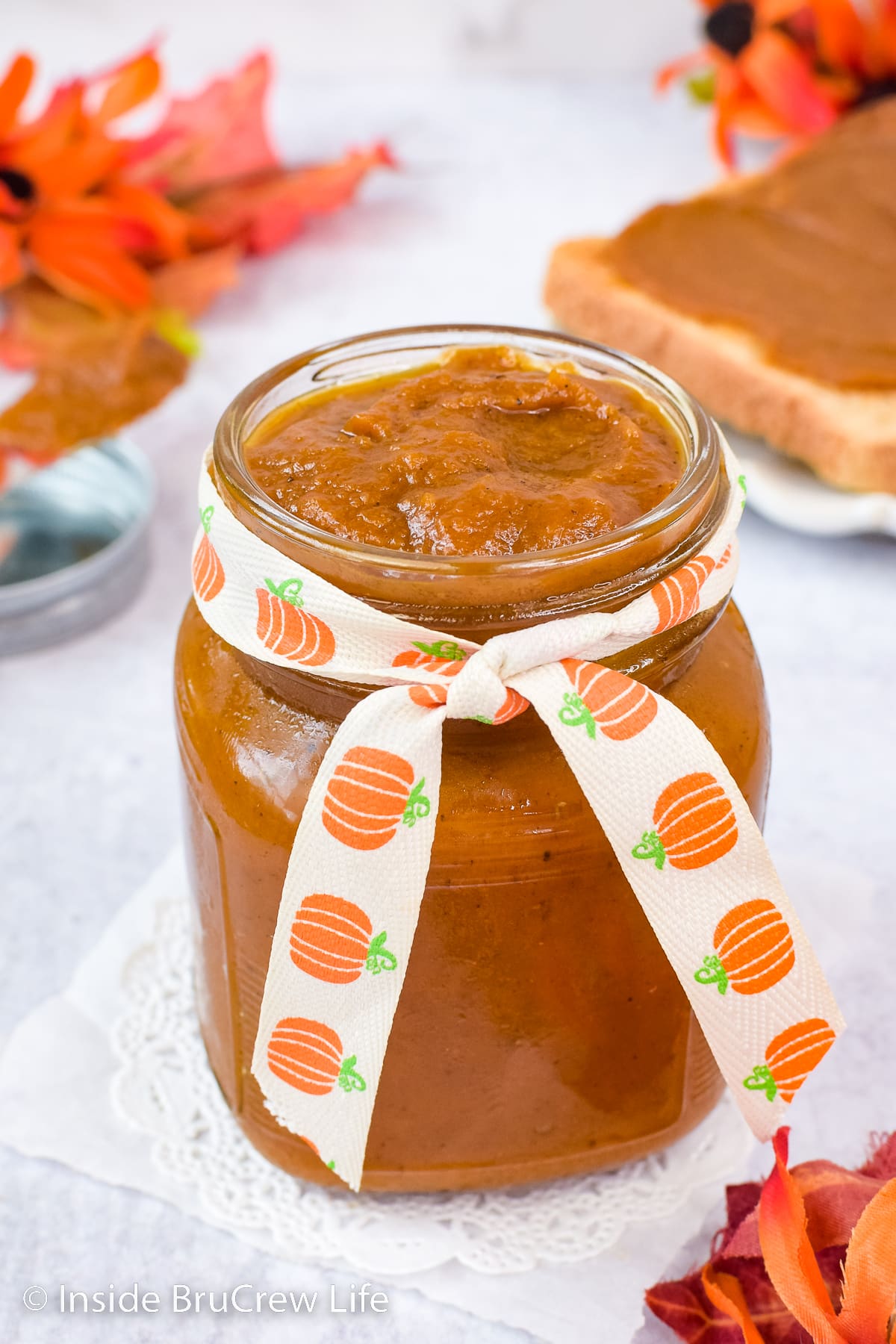 A clear mason jar with a ribbon filled with pumpkin butter.