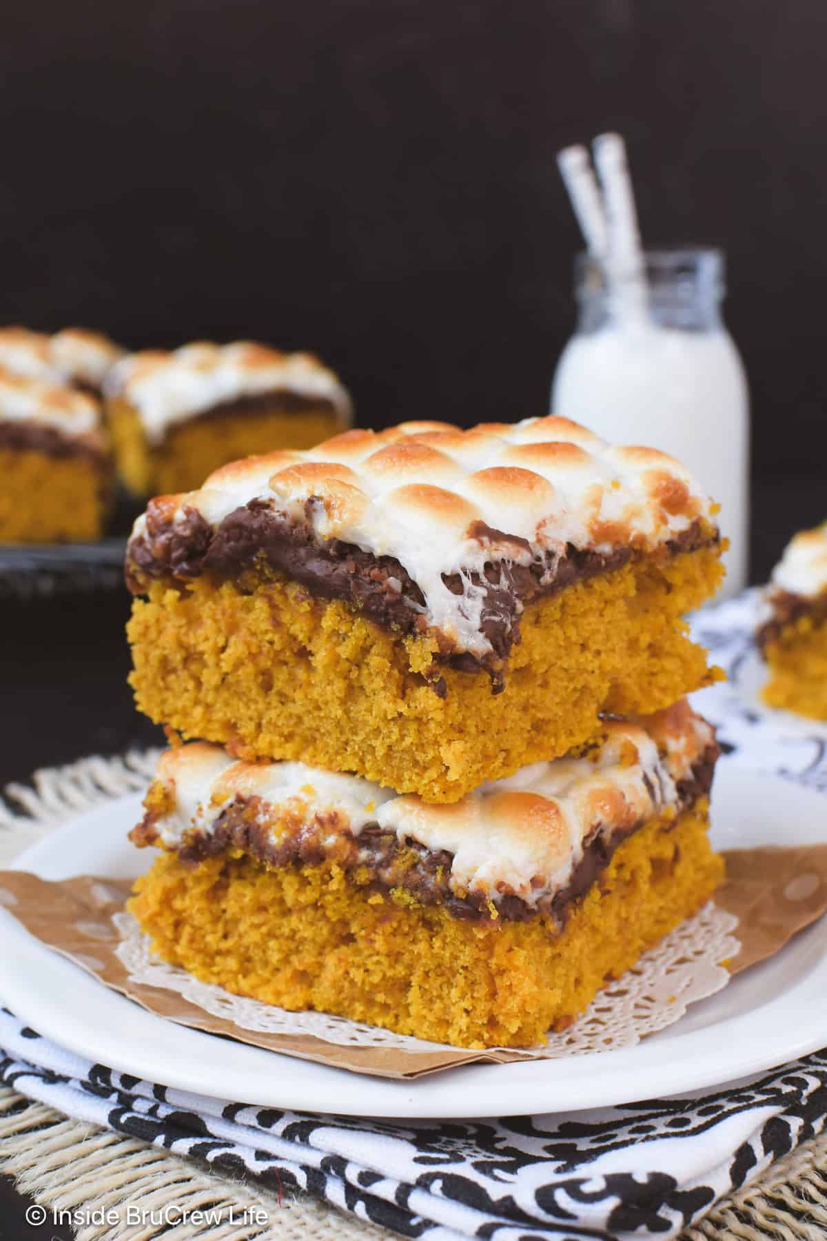 Two s'mores pumpkin bars stacked on a white plate.