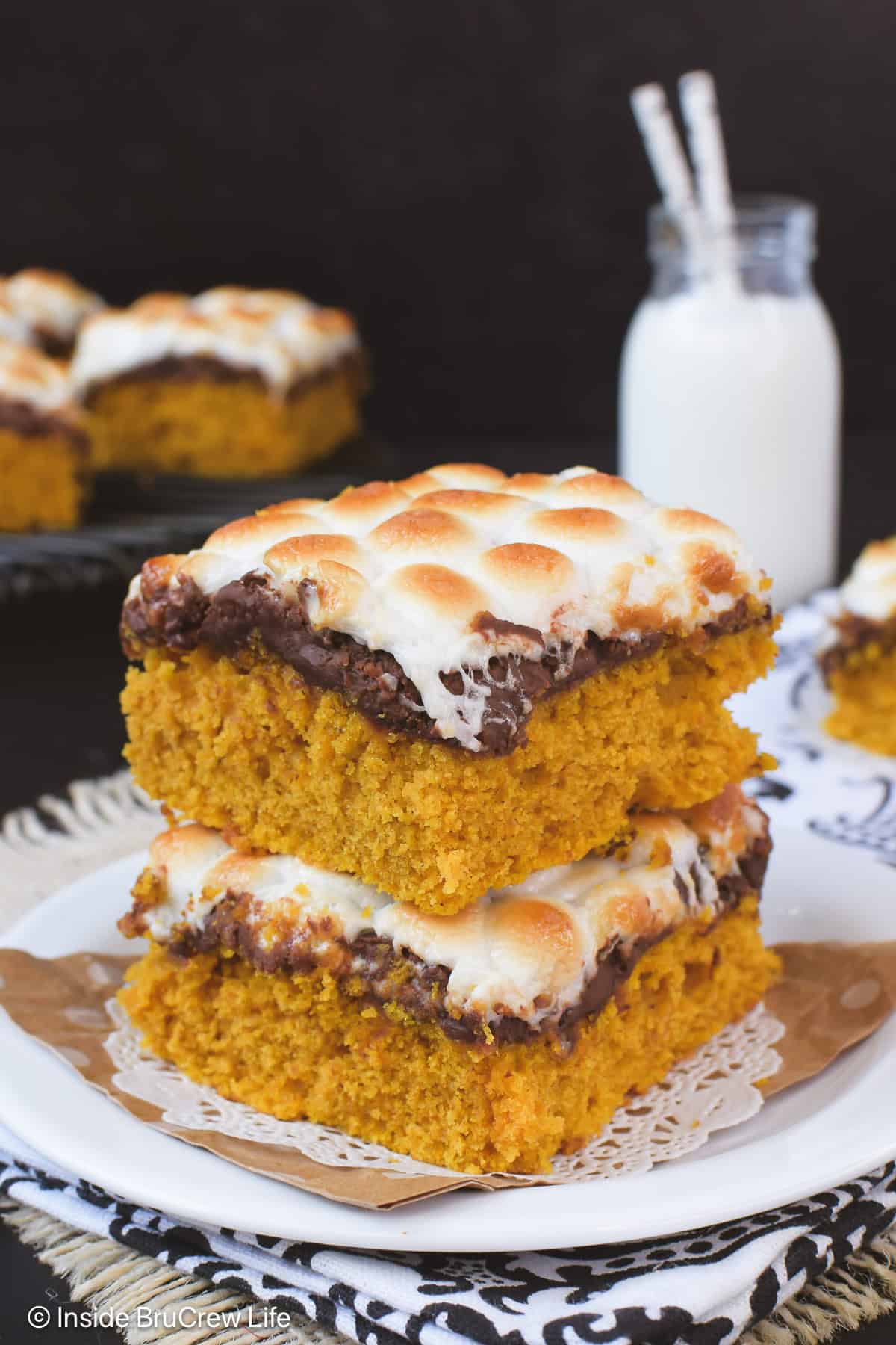Two s'mores pumpkin bars stacked on a white plate.