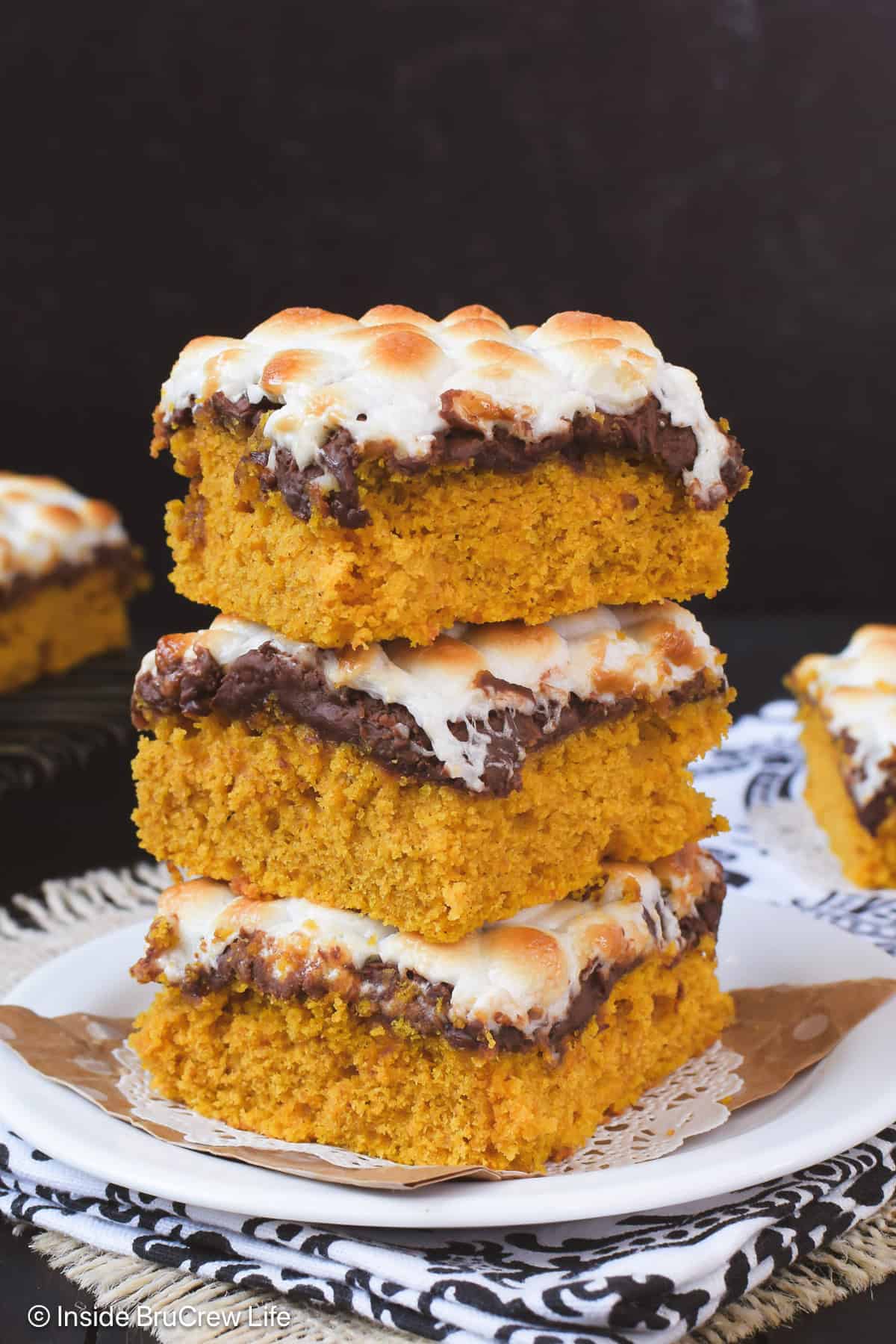 Three pumpkin bars with s'mores toppings stacked on a white plate.