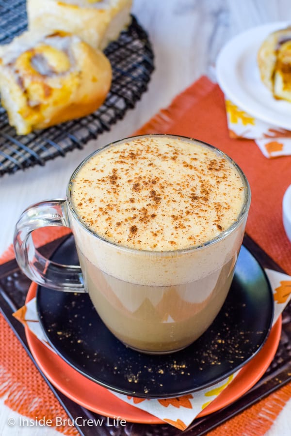 A homemade pumpkin spice latte in a clear mug on a black plate.