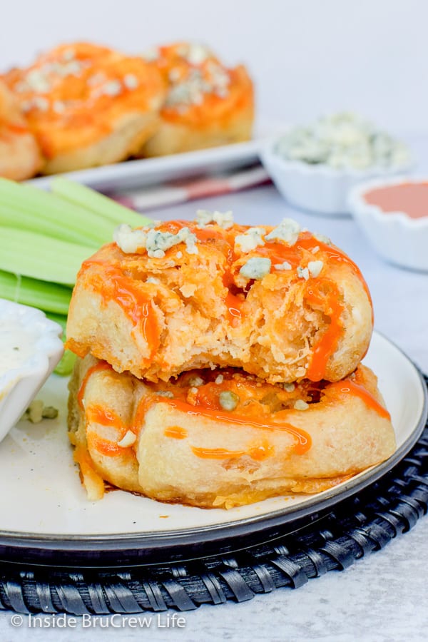 Two buffalo chicken pizza rolls on a plate with dressing and celery and a bite out of the top pizza roll