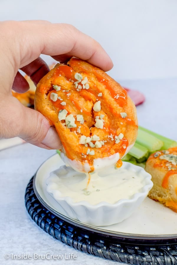 A white bowl filled with ranch dressing with a hand dipping a buffalo chicken pizza roll into it