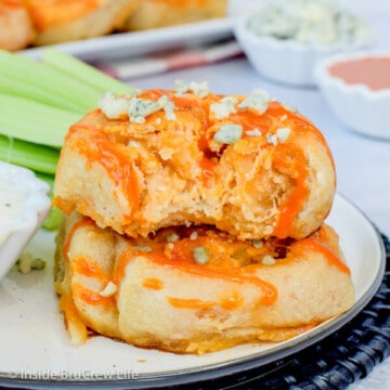 Two buffalo chicken pizza rolls with blue cheese crumbles on top on a white plate and a bite out of the top roll