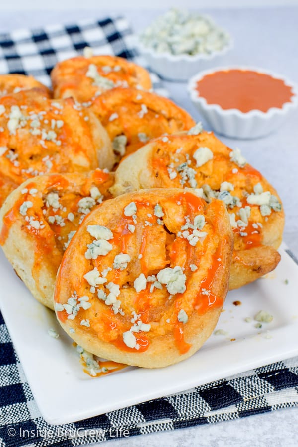 A white plate with buffalo chicken pizza rolls topped with blue cheese stacked on it
