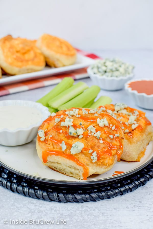 A white plate with two buffalo chicken pizza rolls topped with blue cheese crumbles and wing sauce drizzles on it