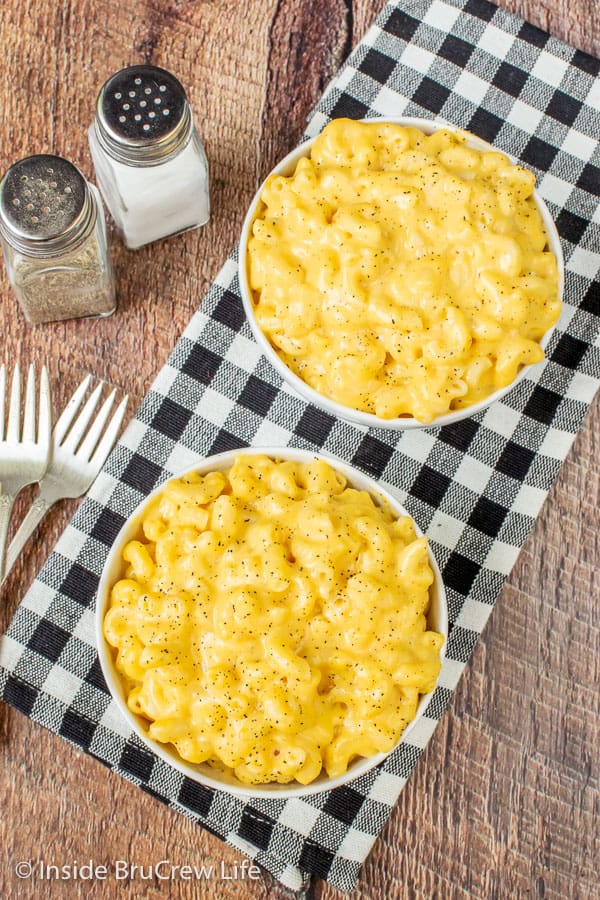 A black and white towel on a board with two white bowls filled with creamy mac and cheese sprinkled with pepper