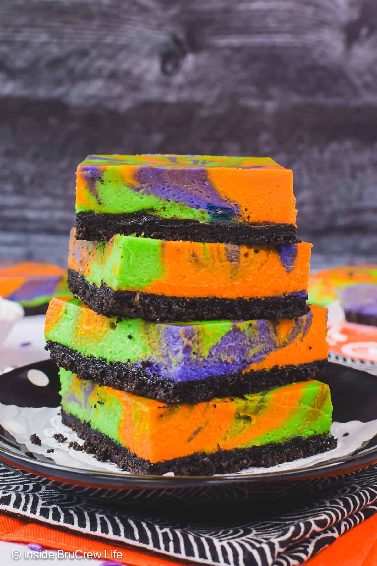 Four Halloween cheesecake bars stacked on top of each other on a black plate.