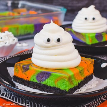 Two swirled cheesecake bars with Cool Whip ghosts on black plates.