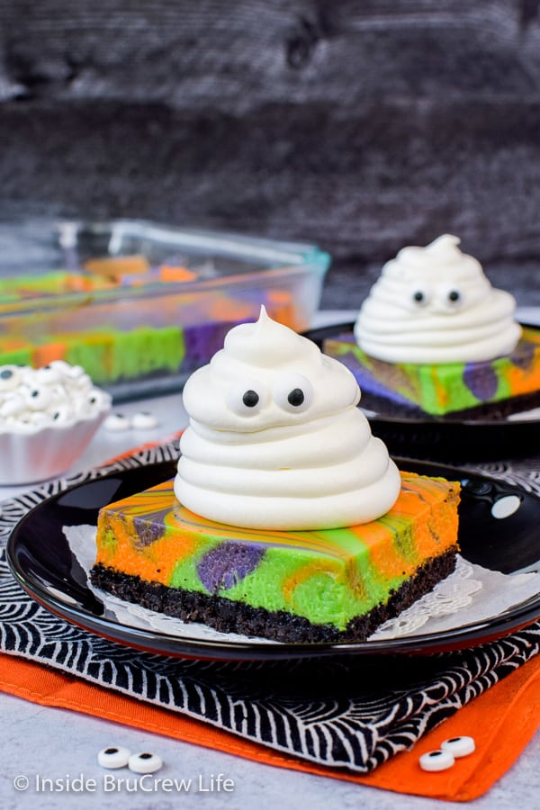 Two black plates with cheesecake bars topped with Cool Whip ghosts.