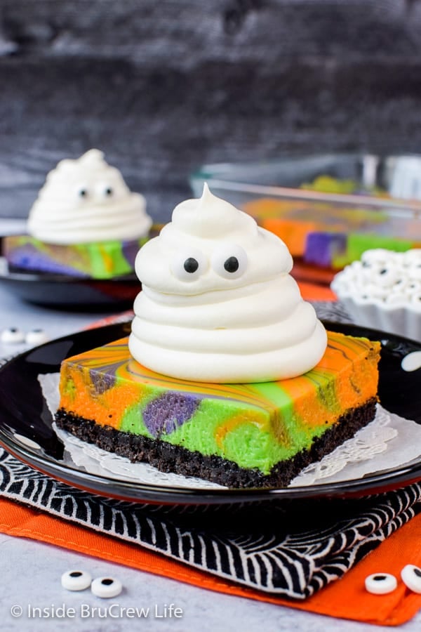 A colorful cheesecake bar topped with a Cool Whip ghost on a black plate.