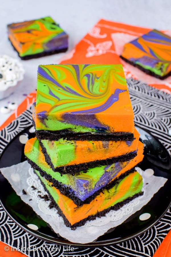 A black plate with a stack of colorful cheesecake bars on it.