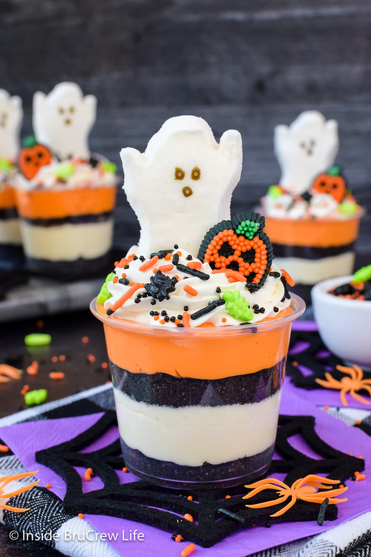 Clear cups filled with colorful cream cheese and Oreo crumbs.