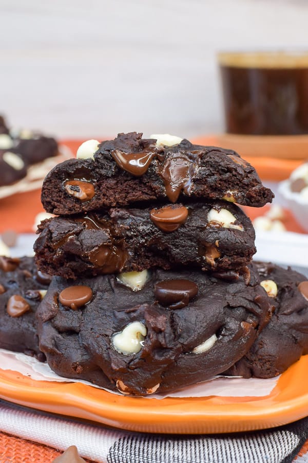 An orange plate with a pile of chocolate pumpkin cookies with one cut in half showing the melty chocolate chips.