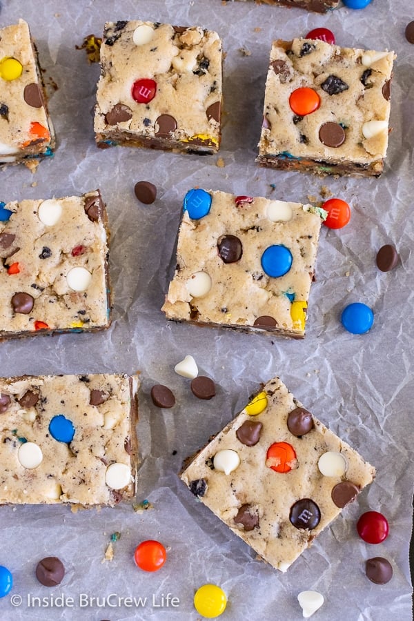 Overhead picture of squares of blondies loaded with candy, chocolate chips, and cookies on a piece of parchment paper