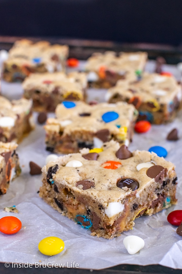 Squares of blonde brownies filled with chocolate, candy, and cookies on a sheet pan