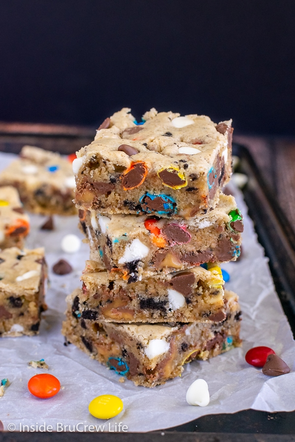 A sheet pan with four blonde brownies stacked on top of each other on it and more behind them