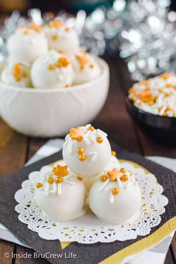 A white doily with white chocolate coated peanut butter balls with yellow sprinkles stacked on it.