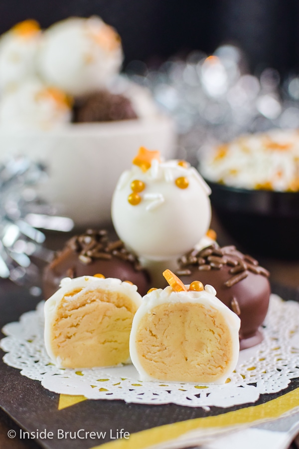 A white doily with peanut butter balls stacked on it and one cut in half in the front showing the creamy center.