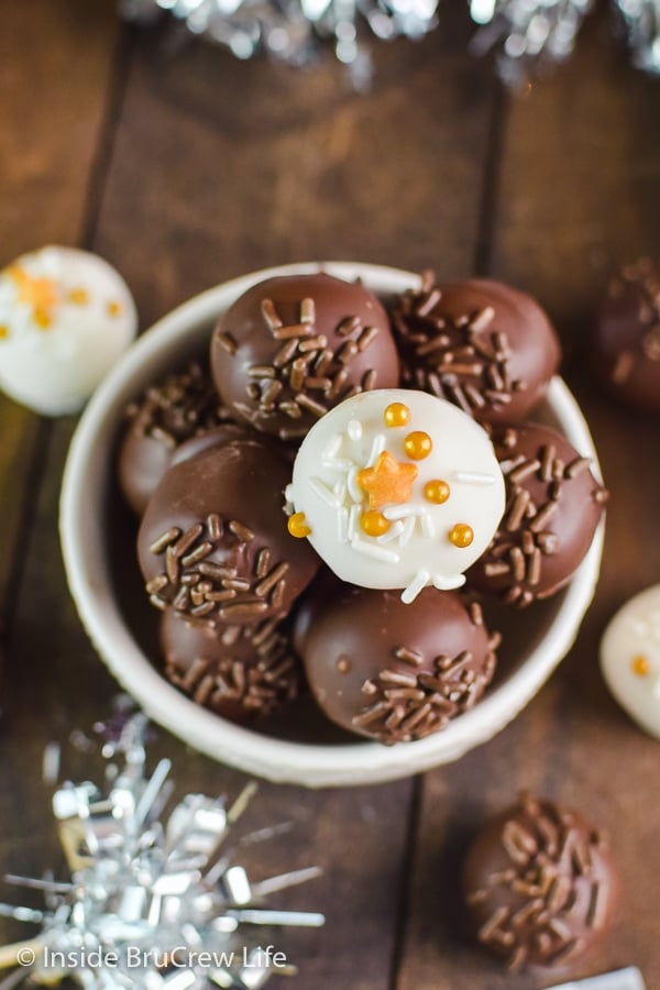 A white bowl filled with peanut butter balls dipped in white and dark chocolate and topped with sprinkles.
