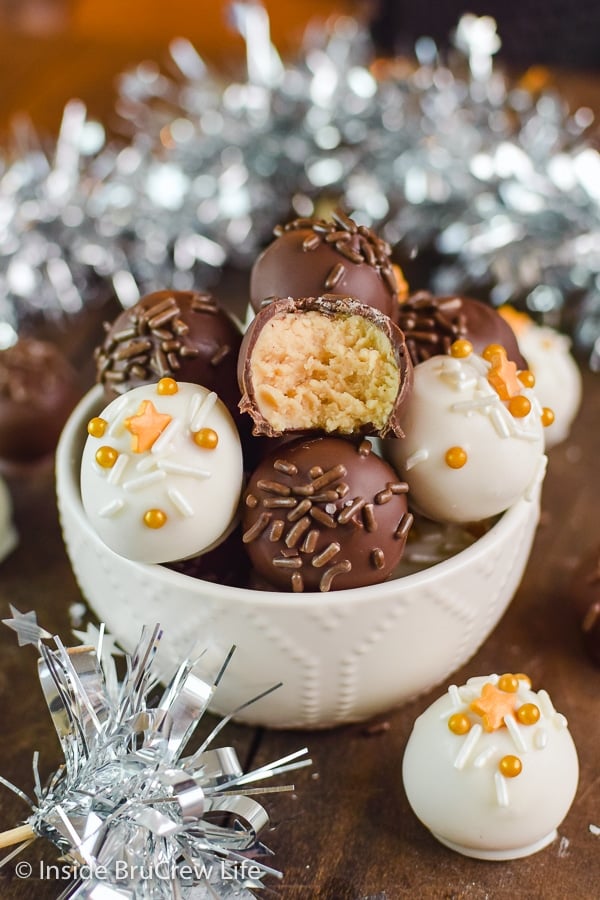 A white bowl surrounded by silver tinsel filled with white and dark chocolate coated peanut butter balls.