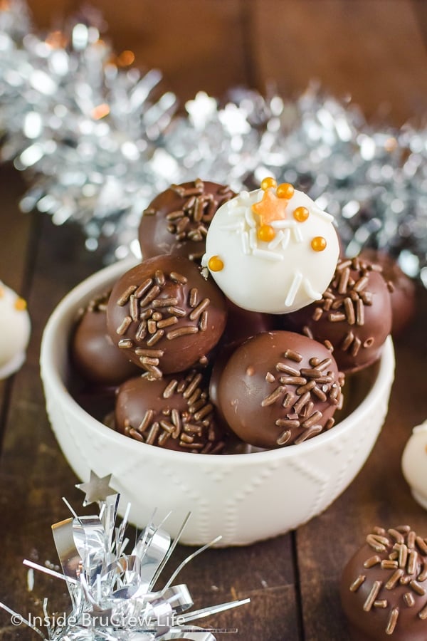 A white bowl on a brown board filled with chocolate covered peanut butter balls with one white one on top.