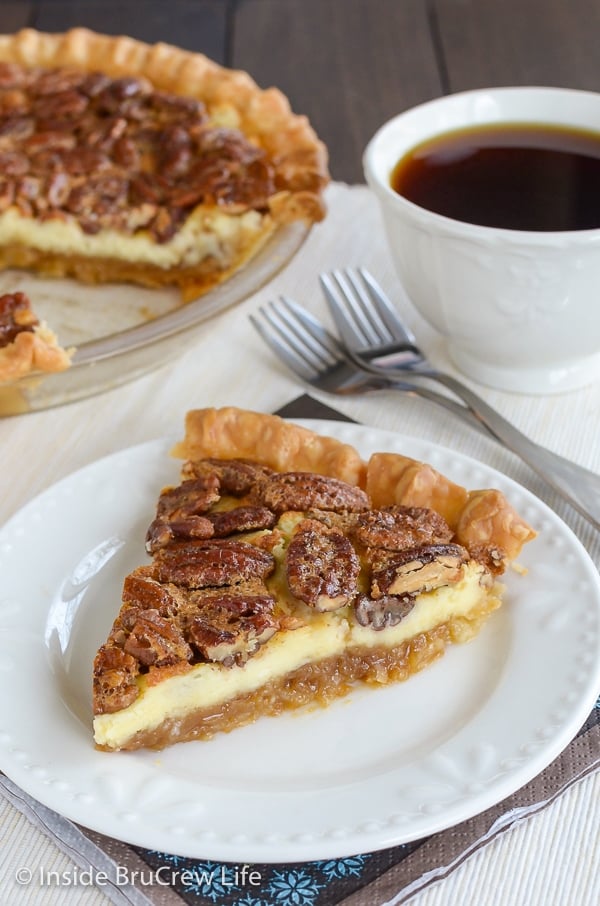 A slice of pecan cheesecake pie on a white plate with a cup of coffee behind it.