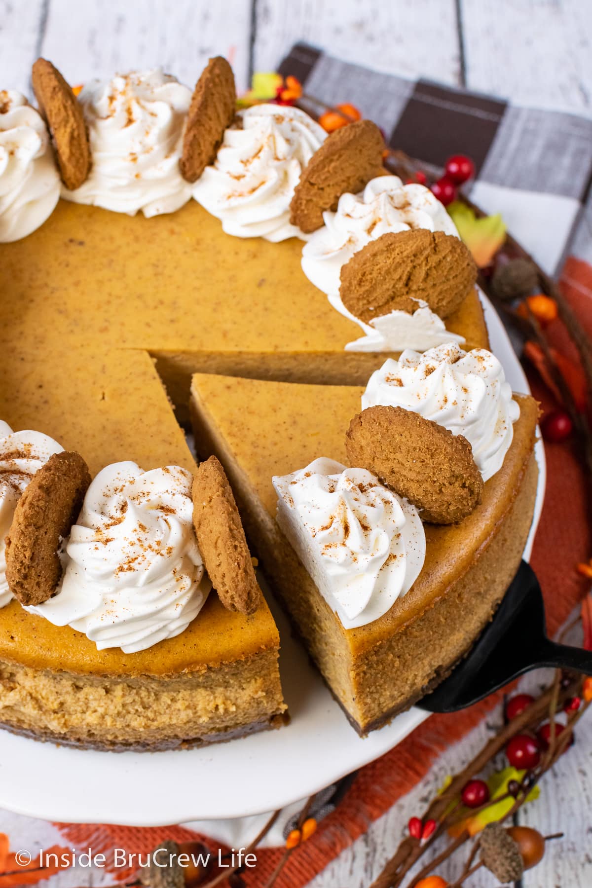 A white cake plate with a full cheesecake decorated with Cool Whip swirls on it.