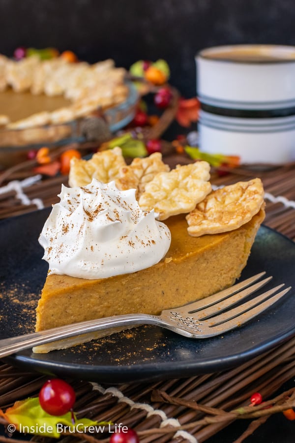 A slice of traditional pumpkin pie with whipped cream and pie crust cookies on a black plate