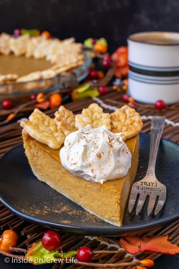 A black plate with a slice of pumpkin pie topped with whipped cream and pie crust cookies on it