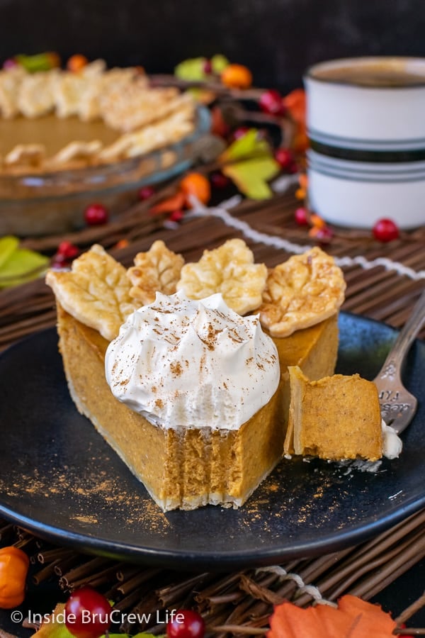 A black plate with a slice of pumpkin pie with whipped cream on it and bite missing from the front of the pie